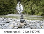 Stack of rocks, cairn, positioned on a pebble beach in front of big waterfall , New Zealand