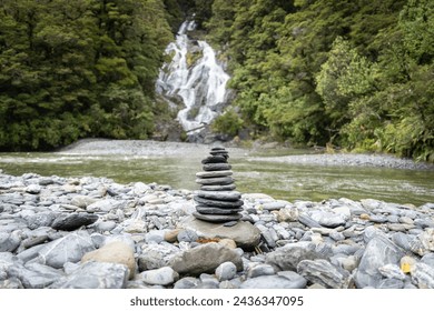 Stack of rocks, cairn, positioned on a pebble beach in front of big waterfall , New Zealand