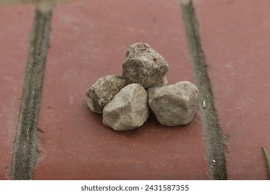 Stack of rocks on brick sidewalk, Pile of stones on red bricks, Rocks arranged on urban walkway, Stones on brick pathway