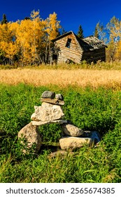 A stack of rocks is sitting in a field next to a house. The house is old and abandoned. The field is lush and green, with tall grass and trees in the background. Concept of solitude and peacefulness
