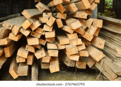 Stack of rough-cut wooden planks piled high outdoors with natural wood grain texture and weathered edges ready for construction or building projects in a rustic outdoor setting.