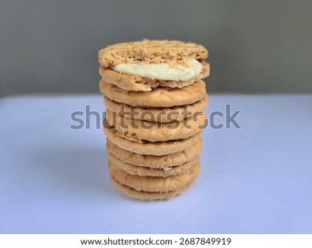 A stack of round, light brown cookies with a creamy filling between the top two cookies. The cookies have a crisscross pattern on them, and the background is a simple gray and white gradient.