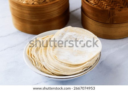 A stack of round and thinly dumpling wrappers or skins, lightly dusted with flour and ready for use. These dough creates a variety of dishes such as dumplings, gyozas, and wonton. 