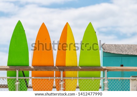Stack row of multicolored colorful stand up surfing boards on railing fence with green orange and yellow color against blue sky lifeguard tower or rental shop