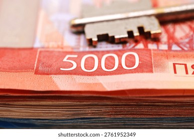 A stack of Russian rubles is shown with a key resting on top. Concept of buying or insuring property with keys and Russian rubles
