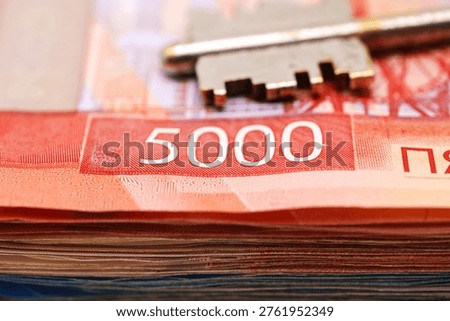A stack of Russian rubles is shown with a key resting on top. Concept of buying or insuring property with keys and Russian rubles