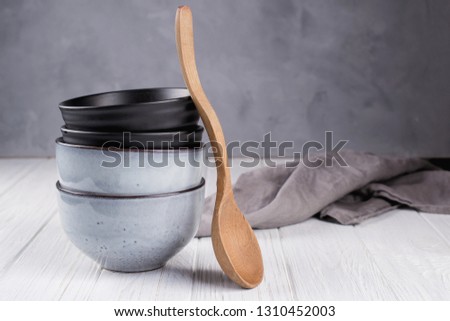 Stack of rustic style handcraft bowls in neutral tones against shabby grey wall with wooden spoon.