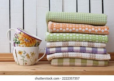 Stack of rustic style kitchen towels and a pair of tea cups on a wooden shelf in a  country house.