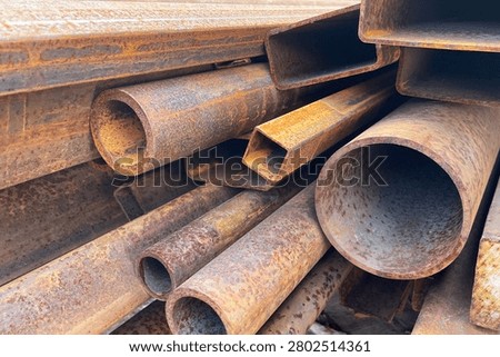 Stack of rusty steel pipes and construction profiles stored outdoors. Corroded industrial materials for metal recycling manufacturing warehouse and heavy industry background concepts.