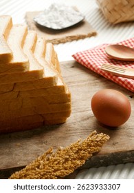 Stack of sandwich bread, on a wooden board, with egg, flour and wheat. Close up.