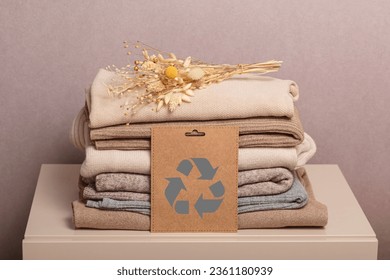 Stack of second hand clothes with used wardrobe for reuse and card with circular economy logo. Reusing, recycling materials and reducing waste in fashion, second hand apparel idea. Zero waste concept