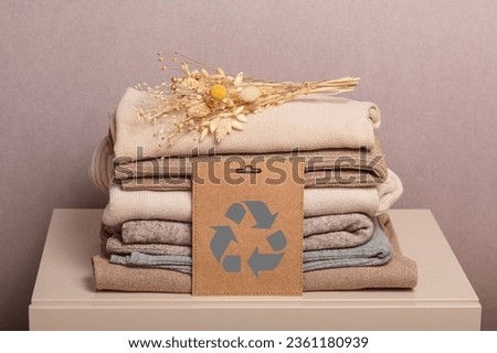 Stack of second hand clothes with used wardrobe for reuse and card with circular economy logo. Reusing, recycling materials and reducing waste in fashion, second hand apparel idea. Zero waste concept