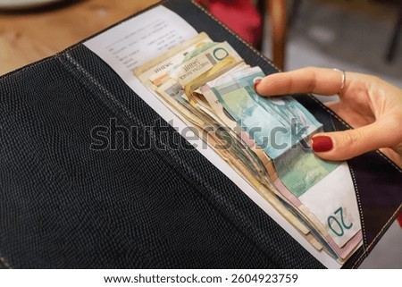 Stack of serbian dinar banknotes left on a restaurant bill inside a black bill folder placed on a wooden table, paying for the meal