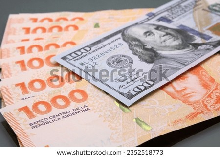 Stack of several thousand Argentine pesos banknotes and one hundred dollar on dark background. Relationship between pesos and dollars, Concept Dolar Blue