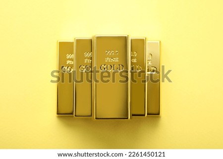 Stack of shiny gold bars on yellow background, top view
