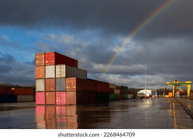 A stack of shipping containers on a deserted commercial dock with sunlight and rainbow
