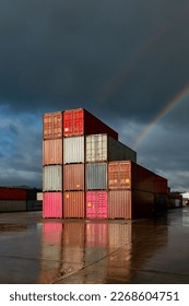 A stack of shipping containers on a deserted commercial dock with sunlight and rainbow