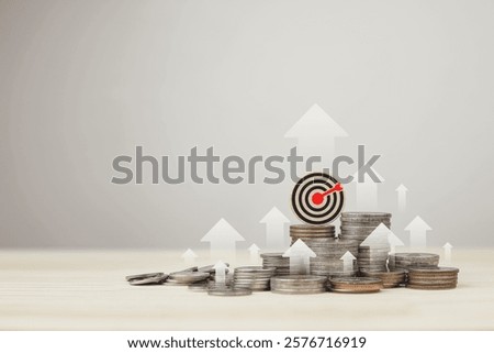 Stack of silver coins,  and target board with rising arrow. Investment management concepts, financial goal planning, accumulating assets for the future, and successful investing.