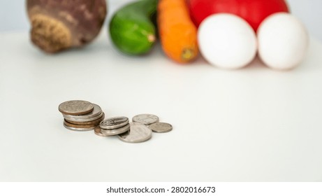 Stack of silver and copper coins on white table with blurred fresh groceries background