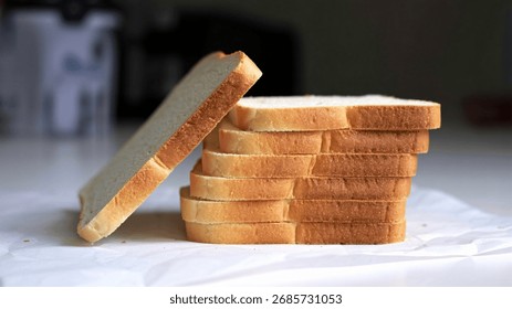 A stack of sliced white bread on a white surface, with one slice leaning against the stack.