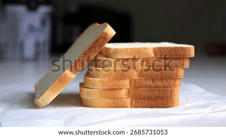 A stack of sliced white bread on a white surface, with one slice leaning against the stack.