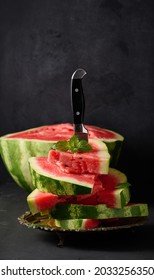 stack of slices of ripe red watermelon in a metal plate, stuck in a large knife. Black background