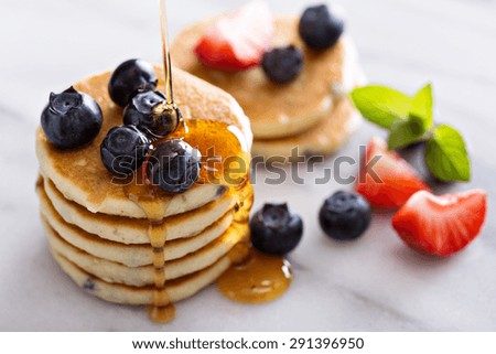 Stack of small pancakes with berries on marble board