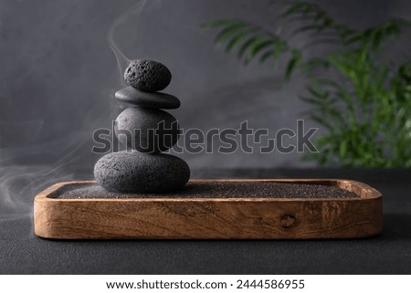 Stack of smooth grey stones balanced in a zen-like arrangement, with a subtle green plant adding a touch of nature, set against a texture grey background, evoking a sense of calm and tranquility. 