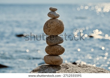 Stack of smooth stones precariously balanced on larger rock by calm seaside, symbolizes balance and serenity, evoking peaceful and meditative atmosphere
