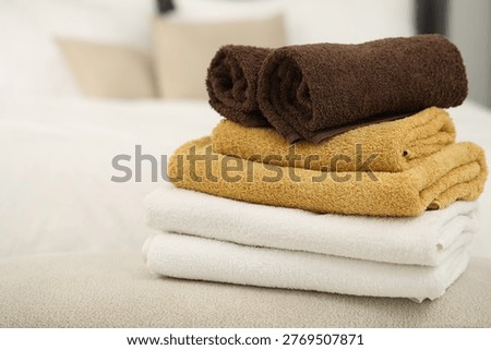 Stack of soft towels on bench near bed indoors, closeup. Space for text