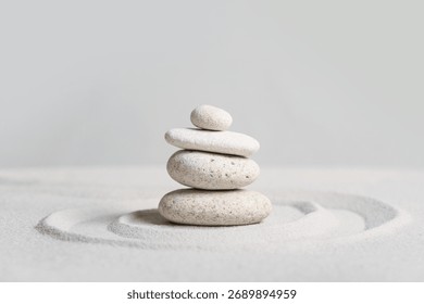 Stack of spa stones on light sand against grey wall. Zen concept
