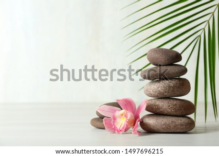Stack of spa stones, palm leaf and flower on table against white background, space for text