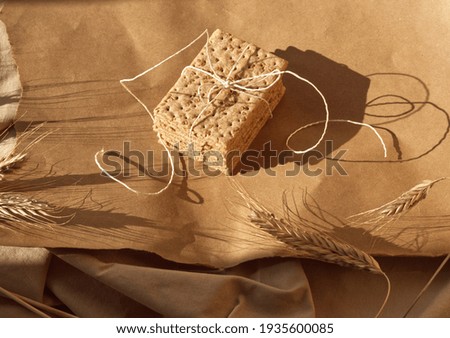 Stack of spelt sesame cracker with ribbon on craft paper background with ears. Minimal food concept. Crispy bread, ray or spelt wheat, sesame seeds. Earth colors, brown tone, monochrome color