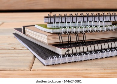 Stack of spiral notebooks on wooden background. Pile of paper notepads with ring binding on wood table. Concept of stationery supplies.