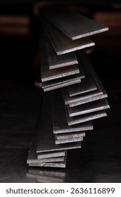 Stack of steel flat bars on a light-reflecting surface, in a dark industrial room, products of the metallurgical industry.