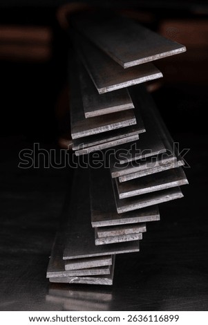 Stack of steel flat bars on a light-reflecting surface, in a dark industrial room, products of the metallurgical industry.