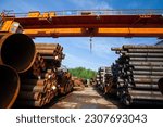 Stack of steel pipes outdoor warehouse. Bridge crane on blue sky background