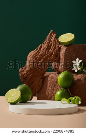 A stack of stones displayed with small white flowers, tree branch, Lime halves and peels. White round podium with empty space for organic product promotion of Lime (Citrus aurantiifolia) extract