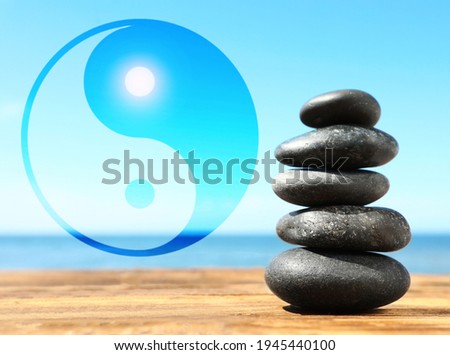 Stack of stones on wooden table outdoors and Ying Yang symbol. Feng Shui philosophy 