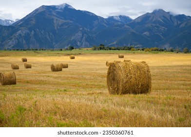 Stack of straw on the mown field beneath a blue sky and high mountains.