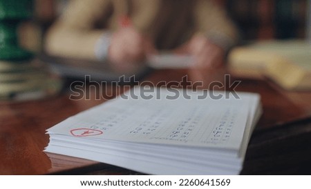 Stack of students test papers lying on teacher's desk, A grade on top sheet