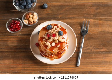 Stack of tasty pancakes with berries, nuts and syrup on table, top view