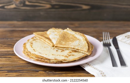 A stack of thin pancakes on a plate and cutlery on a linen napkin in a rustic style. Selective focus.