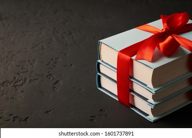A stack of three books tied with a red ribbon with a bow on a dark background about a place for text: concept of a good book - a good gift.