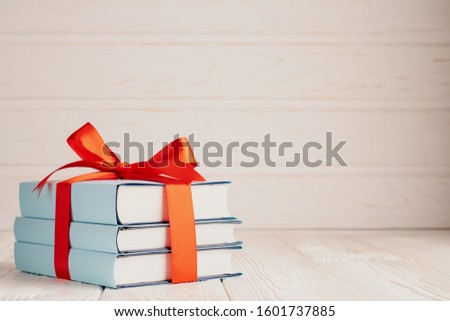 A stack of three books tied with a red ribbon with a bow and copy space: the concept of a good book - a good gift.