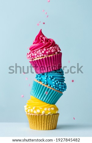 Stack of three colorful cupcakes with falling sprinkles