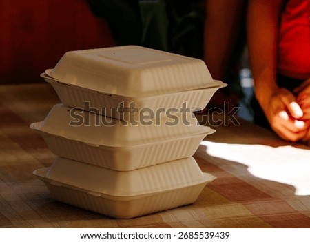 Stack of three eco-friendly biodegradable takeout containers on table with blurred background.