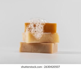 Stack of three handmade natural soap bars with foam and bubbles on a white background. Clean and minimalistic composition. Ideal for eco, skincare, and wellness concepts.