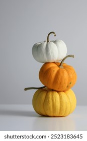 A stack of three pumpkins in white, orange, and yellow sits on a clean, minimal surface, highlighting the vibrant colors typical of the autumn harvest season.