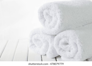 Stack Of Three Rolls Of White Fluffy Bath Towels On The Background Of White Boards